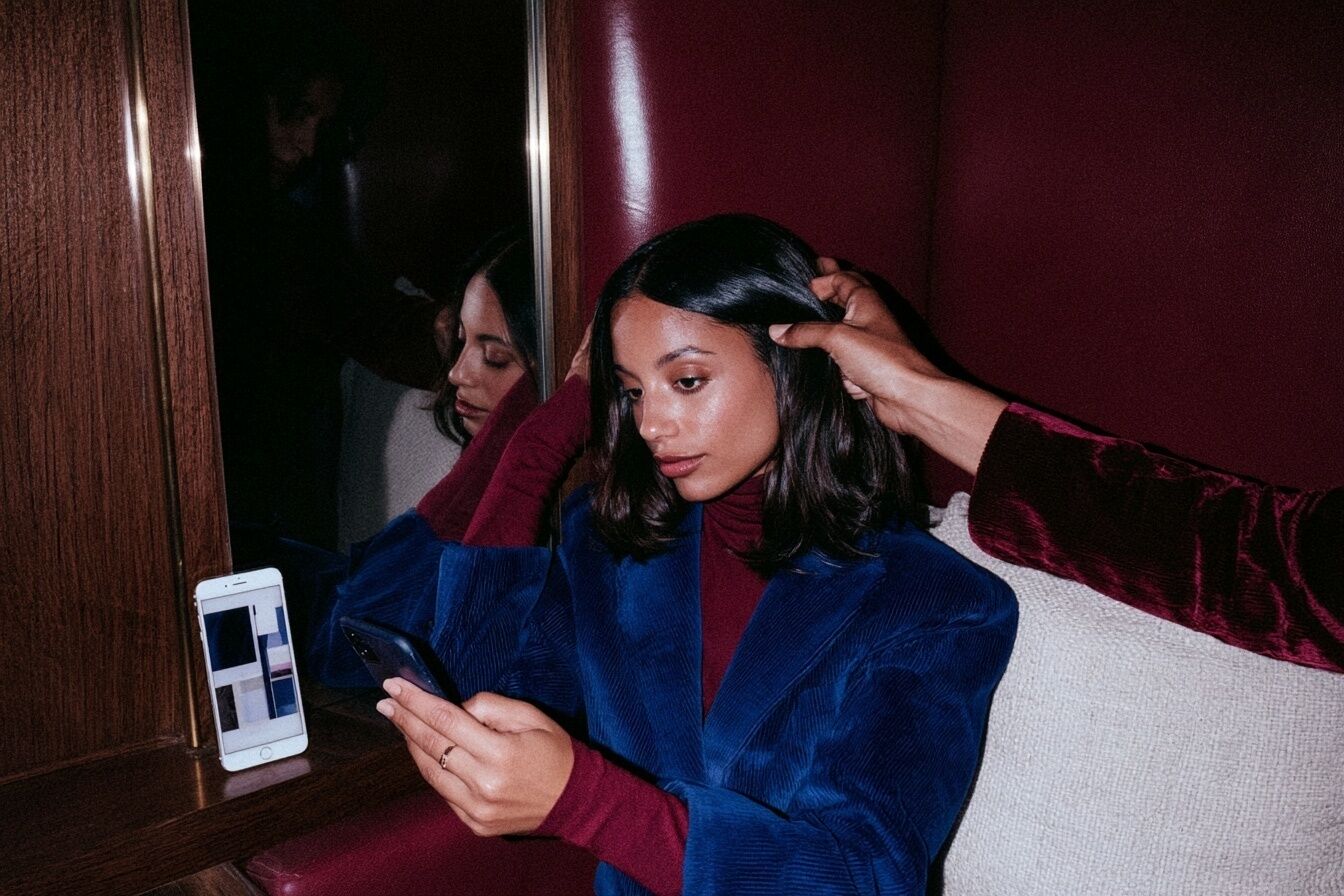 Eine Kundin betrachtet Frisuren-Inspiration auf dem Smartphone, während die Stylistin ihren fertigen Look prüft.